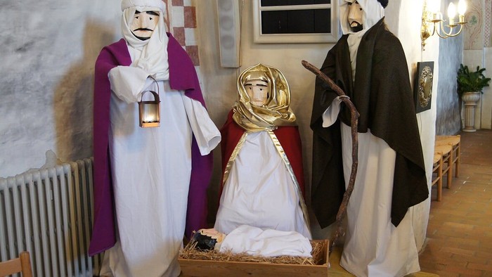 Tre skikkelser i traditionelle klæder, en med lygte, en med barn og en med stav.