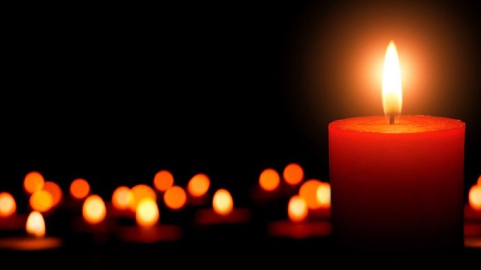 Ein einzelnes rotes Kerzenlicht steht prominent vor vielen kleineren Kerzen im Hintergrund.