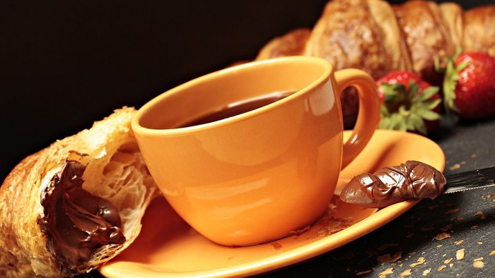 Ein orange Tasse mit Kaffee und ein Croissant mit Schokolade auf einem Teller