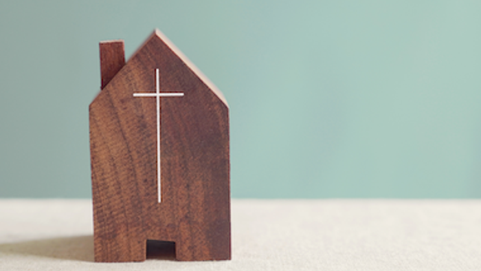 Ein hölzernes Modell einer Kirche mit Kreuz vor hellblauem Hintergrund