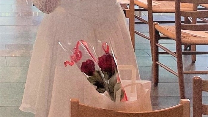 En kvinde står med ryggen til kameraet med en blomsterafsnit i håret.