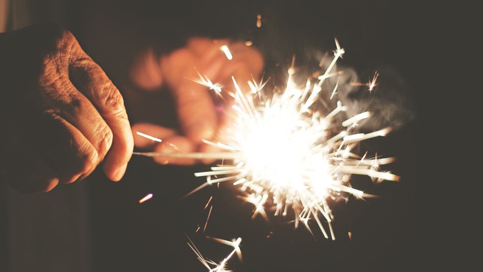 En hånd holder en bengel med lysende fyrværkeri i mørket.