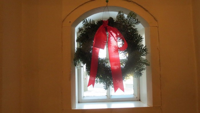 En julekrans med rød bue hænger i et vindueskarm