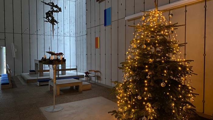 En juletree med lys og pynt i et rum med benker og kunst.