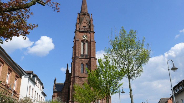 Hohe Kirchturmspitze vor blauem Himmel und Gebäuden
