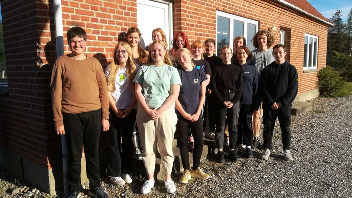 En gruppe unge står foran et rødt murstenshus.