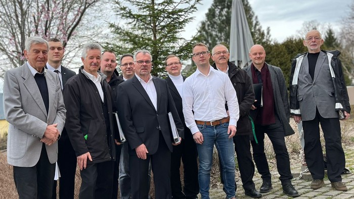 Eine Gruppe von Männern posiert vor einem Baum und einem Denkmal