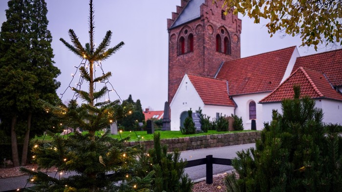 En juletree foran en kirke med tårn og røde tag.
