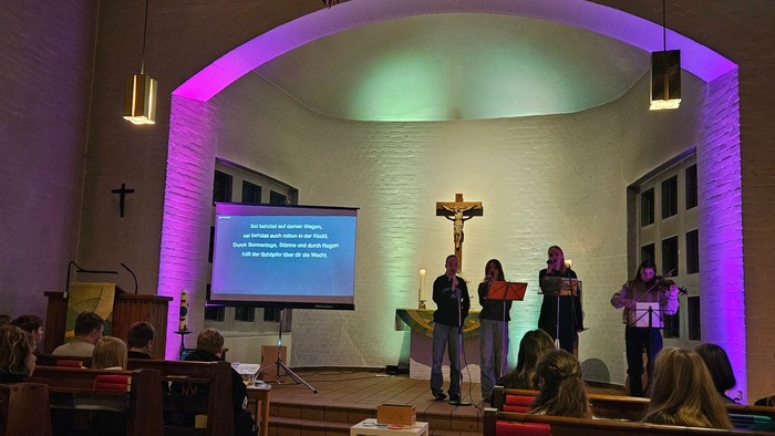 In der Kirche findet eine Veranstaltung statt, Menschen stehen vor einem Bildschirm und einem Kreuz.
