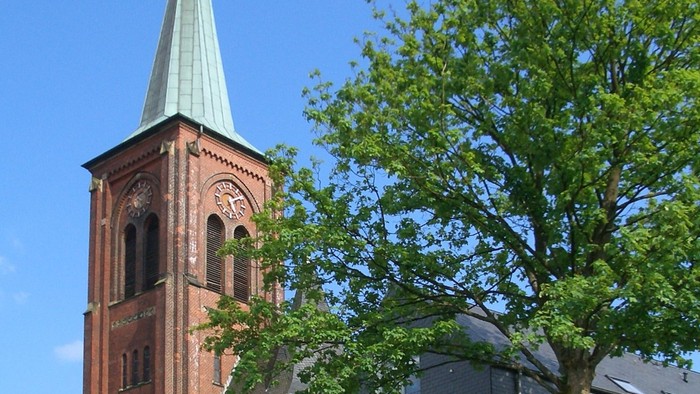 Kirchturm aus rotem Backstein neben einem Baum