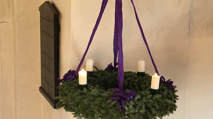 En adventskrans med to levende lys hængt op med lilla bånd.