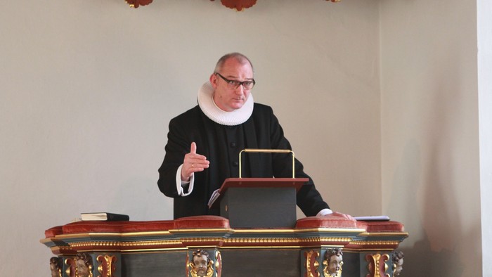 En præst i svart drømmer til et bord med boger.