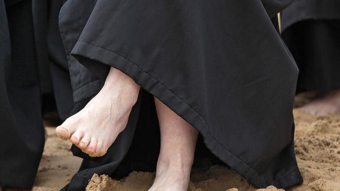 Person in schwarzer Robe kniet im Sand