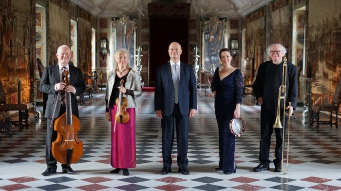 En gruppe af klassiske musikere i formelt tøj spiller i en prægtig sal.