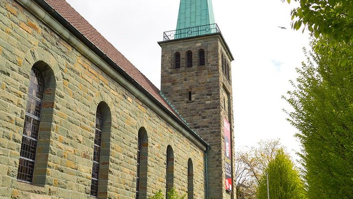 Historische Steinkirche mit hohem Turm in einer üppigen, grünen Landschaftsgestaltung.