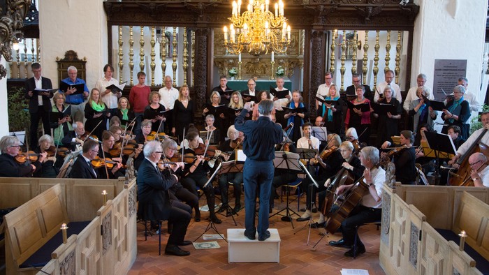 En symfoniorkester optræder i en stor sal med publikum.