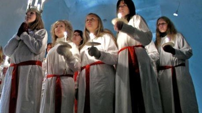 En gruppe kvinder i hvide kler med røde bælter står sammen og ser opad.