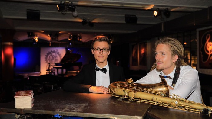 Zwei Männer in Smokingjacken spielen Saxophone in einer Bar