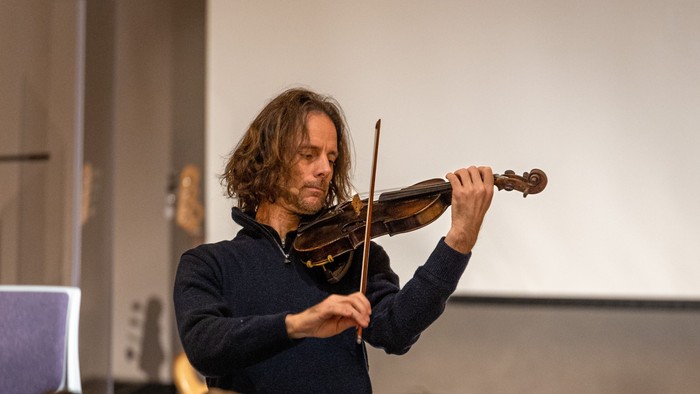 Ein Mann spielt Geige vor einem Publikum in einem Raum.