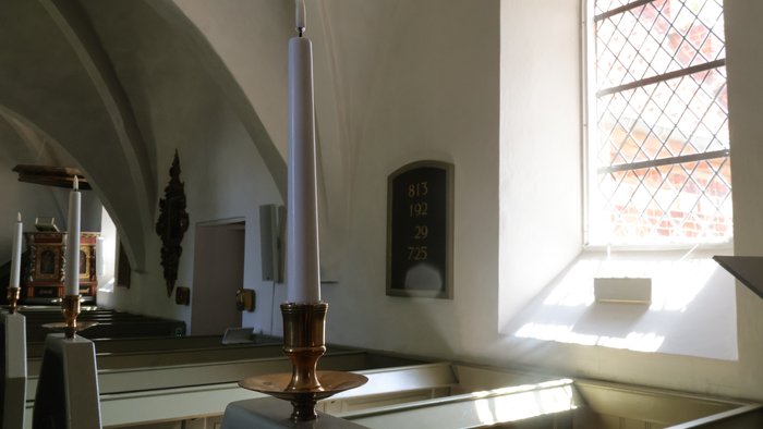 Inden i gammel kirke med altertavle og lysende vindue.