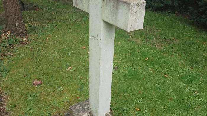 En hvid korsformet gravsten på en grøn eng.