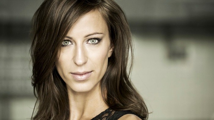 En kvinde med langt, mørkt hår og blå øjne ser direkte i kameraet.