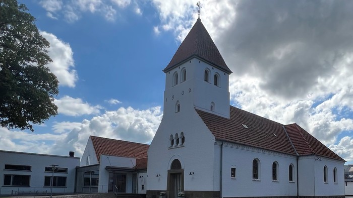 Hvid kirke med tårn og røde tag under blå himmel med skyer