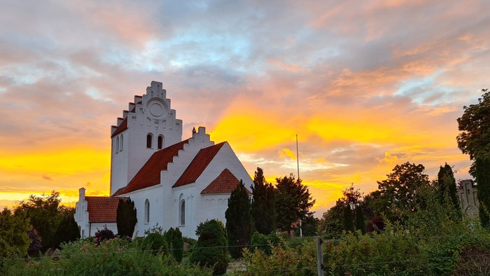 En hvid kirke med røde tag ved solnedgang