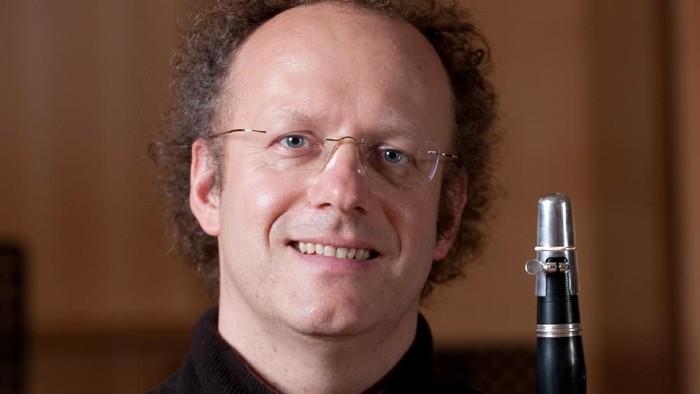 Ein Mann mit Brille hält ein Klarinette und lächelt.