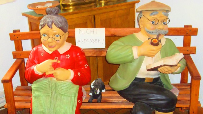 Zwei geschnitzte Figuren sitzen auf einer Bank und stricken.