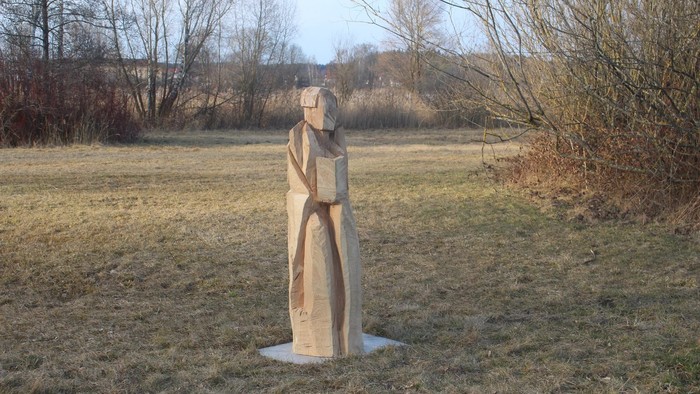 Im Feld steht eine Holzskulptur einer Frau mit Buch.