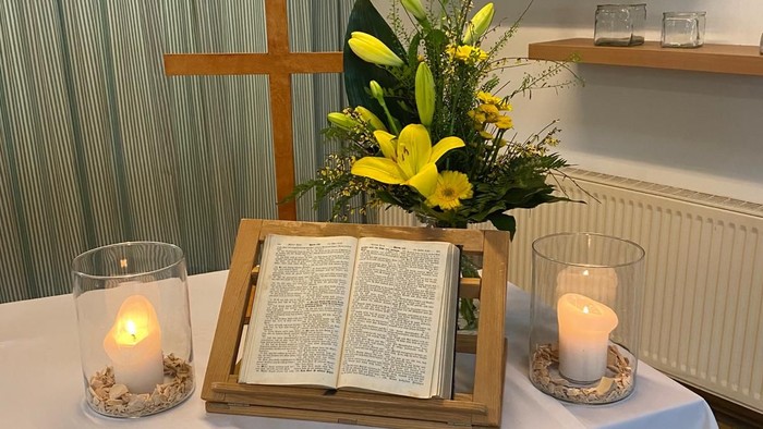 Ein Tisch mit Kerzen, Kreuz, Buch und Blumenarrangement