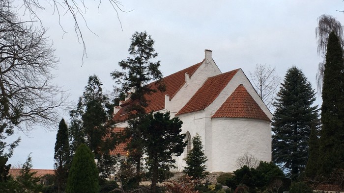 Hvid kirke med rødt tag og omgivet af træer og buske