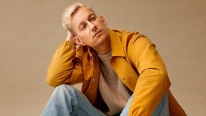 En kvinde i guldgul jacke og blåjeans sidder og tænker.