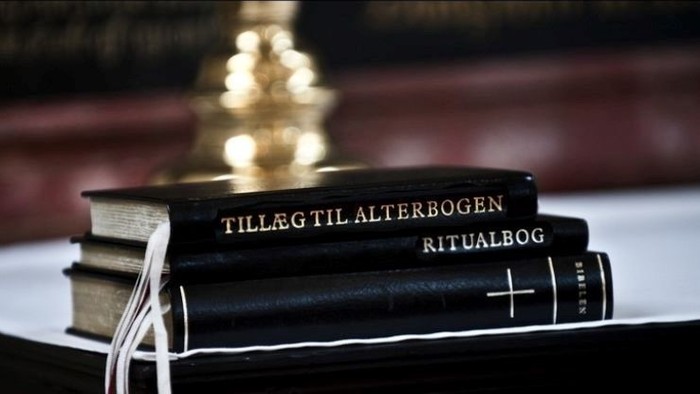 To books titled "Tilleg til alterbogen" and "Ritualbog" placed on a table with a blurred Christmas tree in the background.