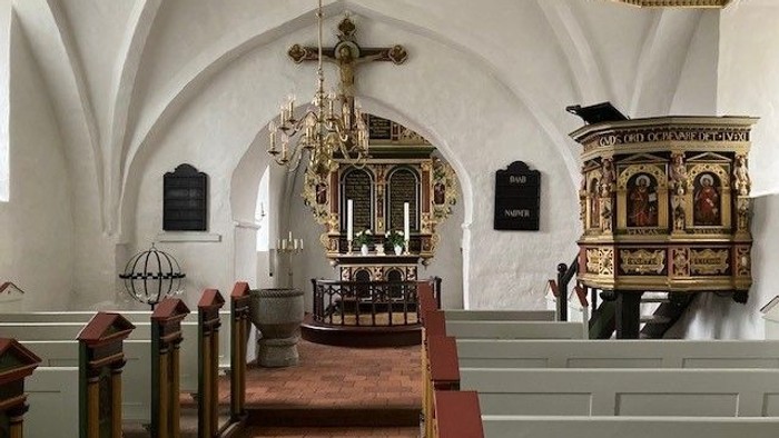 Indre del af kirke med alter, bænke og hængende lygte.