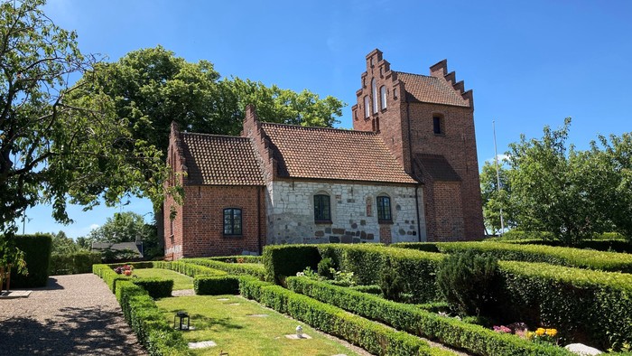 Et rødt teglmurstenshus med tårn og omgivet af en managtaget have