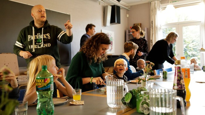 En gruppe af voksne og børn sidder ved et langt bord og spiser.
