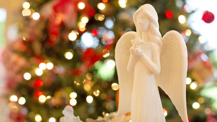 En hvid engelstatue foran en julested med lys og pynt.