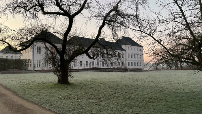 En stor, hvid bygning med many tømrer i en parkagtig omgivelse ved solnedgang