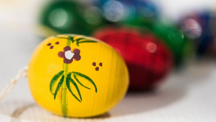 Billedet viser en gult æble med malet blomst og blad, omgivet af andre farvede æbler.