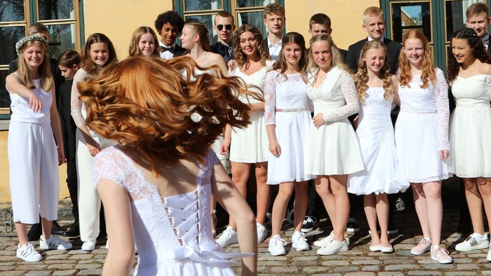 En gruppe kvinder i hvide tøjer og mænd i formelle klæder står på en fladt pave.