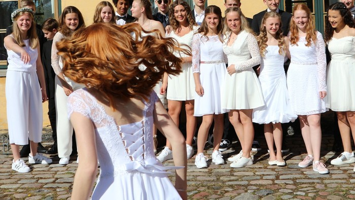 En gruppe kvinder i hvide tøjer og mænd i formelle klæder står på en fladt pave.