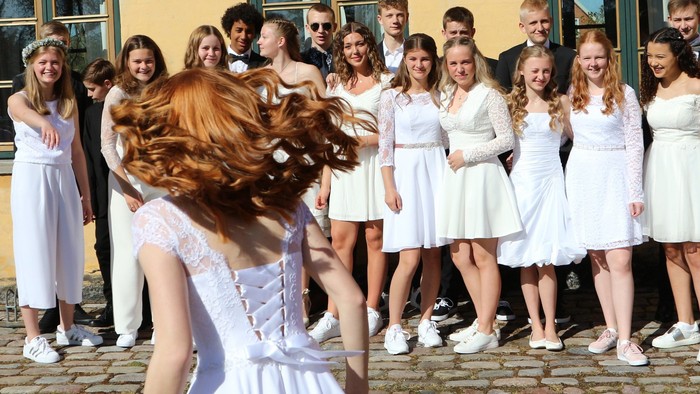 En gruppe kvinder i hvide tøjer og mænd i formelle klæder står på en fladt pave.