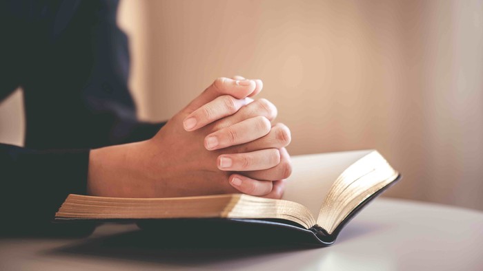 Hände gefaltet auf aufgeschlagenem Buch