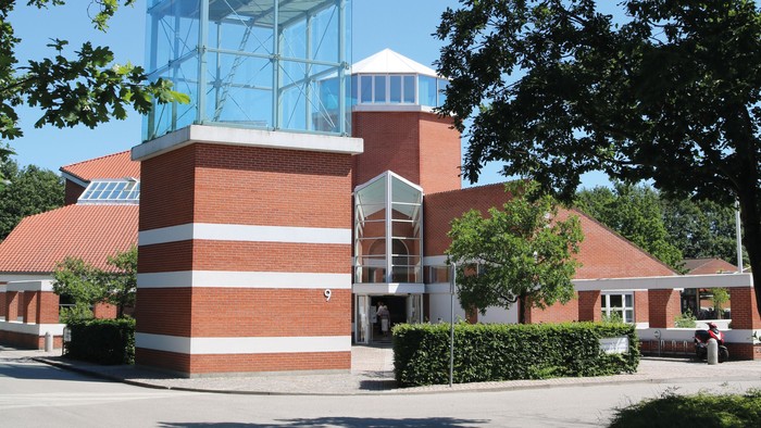 Et moderne glasbygning i en parkagtig omgivelse