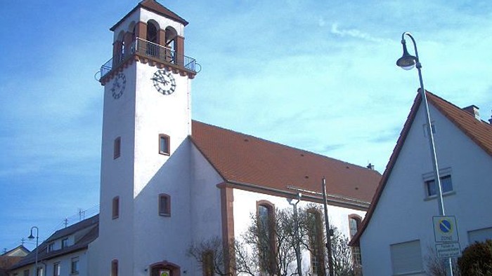 Weiße Kirche mit hohem Turm und Uhr, rote Ziegeldächer, klarer blauer Himmel