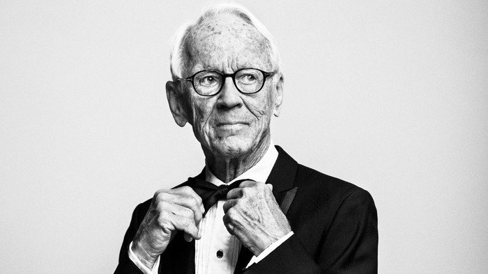 En eldre mand i formel klædning justerer sin knap.