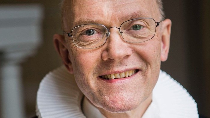 En smilende, eldre mand med glas og en hvid krage.