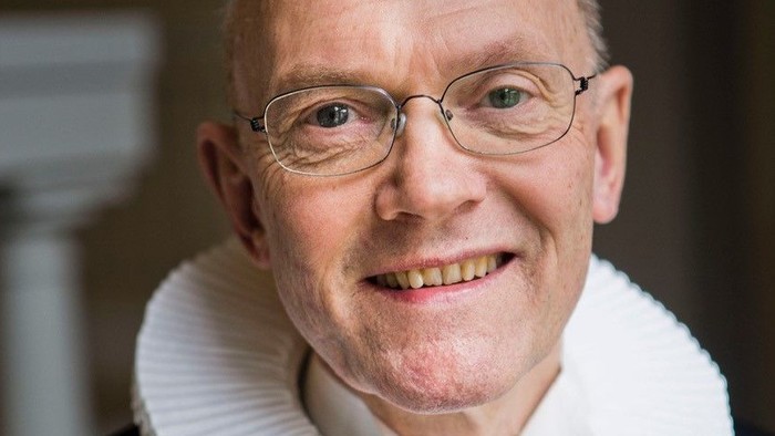 En smilende, eldre mand med glas og en hvid krage.